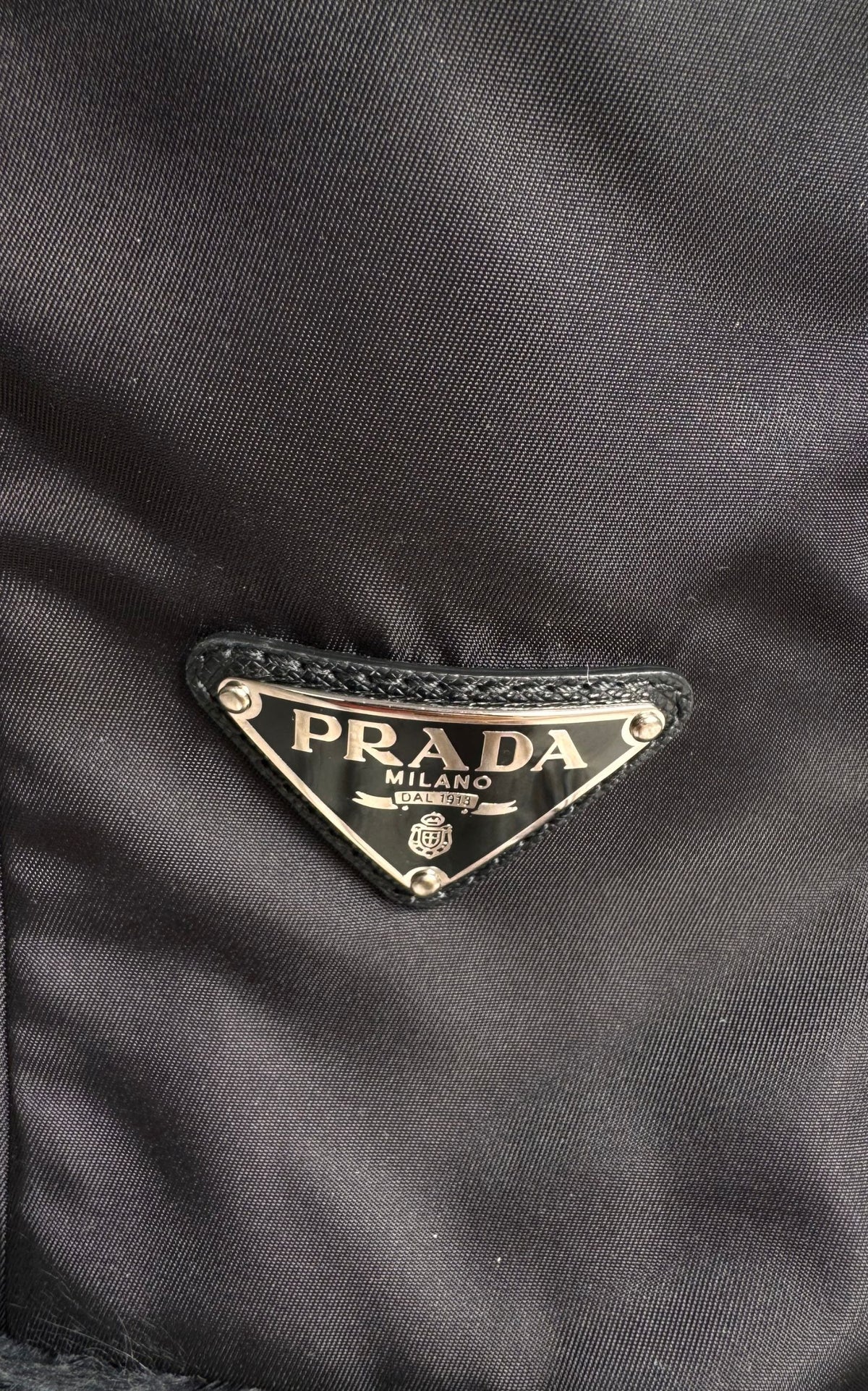 Close-up of a black Prada nylon fabric with the iconic triangular metal logo plaque on the front.