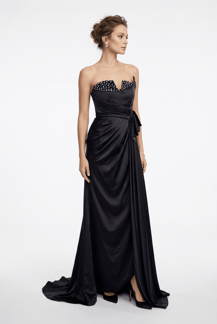 A woman modeling a strapless black satin evening gown with a sweetheart neckline, embellished bodice, draped waist, and floor-length train against a light gray studio background.