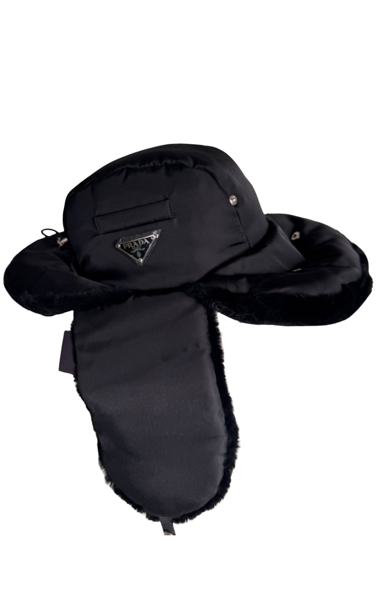 A black winter trapper hat with plush ear flaps and a faux-fur trim, featuring a small silver-tone triangular Prada logo on the front.