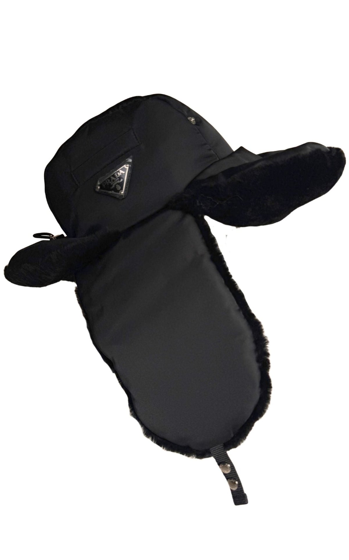 A black Prada winter trapper hat with plush ear flaps and a chin strap, featuring a small triangular logo patch on the side, set against a plain white background.