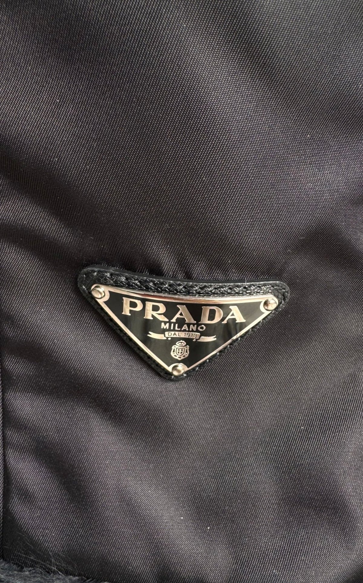 Close-up of a black Prada nylon fabric with the iconic triangular metal logo plaque on the front.