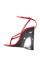 Alaia red patent leather wedge sandal with a sculptural, hollowed-out black wedge heel and thin red straps, shown from a side profile on a white background.