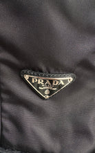 Close-up of a black Prada nylon fabric with the iconic triangular metal logo plaque on the front.