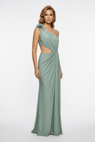 A woman modeling a floor-length one-shoulder gown in a muted sage green color. The dress features a twisted draping detail at the waist and a matching fabric flower accent on the shoulder, set against a plain white studio background.