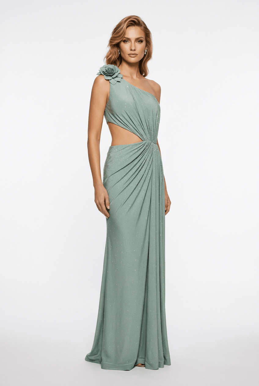 A woman modeling a floor-length one-shoulder gown in a muted sage green color. The dress features a twisted draping detail at the waist and a matching fabric flower accent on the shoulder, set against a plain white studio background.