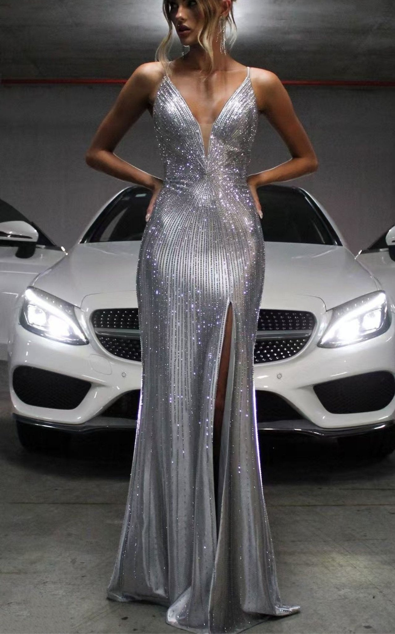 Silver rhinestone mermaid formal dress v plunge front view on a model posing in front of a Mercedes