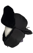 A black Prada winter trapper hat with plush faux-fur ear flaps and chin coverage, displayed on a white mannequin head against a plain white background.