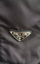 Close-up of a black Prada nylon fabric with the iconic triangular metal logo plaque on the front.