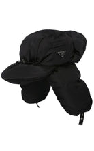A black Prada winter trapper hat with ear flaps and chin cord, featuring a small triangular Prada logo on the side, set against a plain white background.