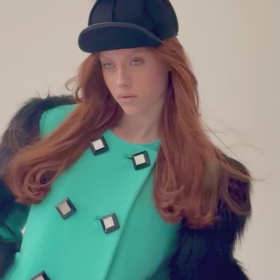 Woman wearing a Gucci green overcoat with black faux fur sleeves and bog buttons,