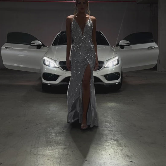 Silver rhinestone mermaid formal dress v plunge front view on a model posing in front of a Mercedes