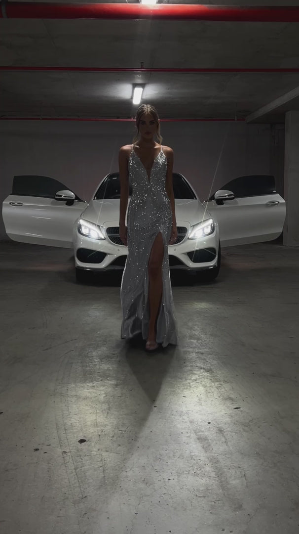 Silver rhinestone mermaid formal dress v plunge front view on a model posing in front of a Mercedes