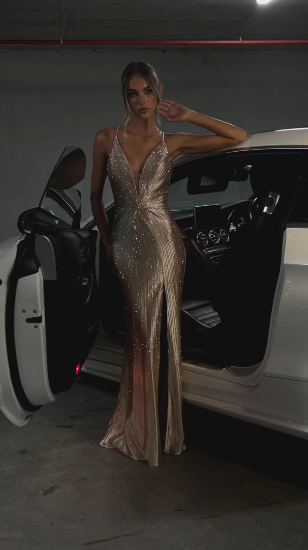 Gold rhinestone mermaid formal dress v plunge front view on a model posing in front of a car